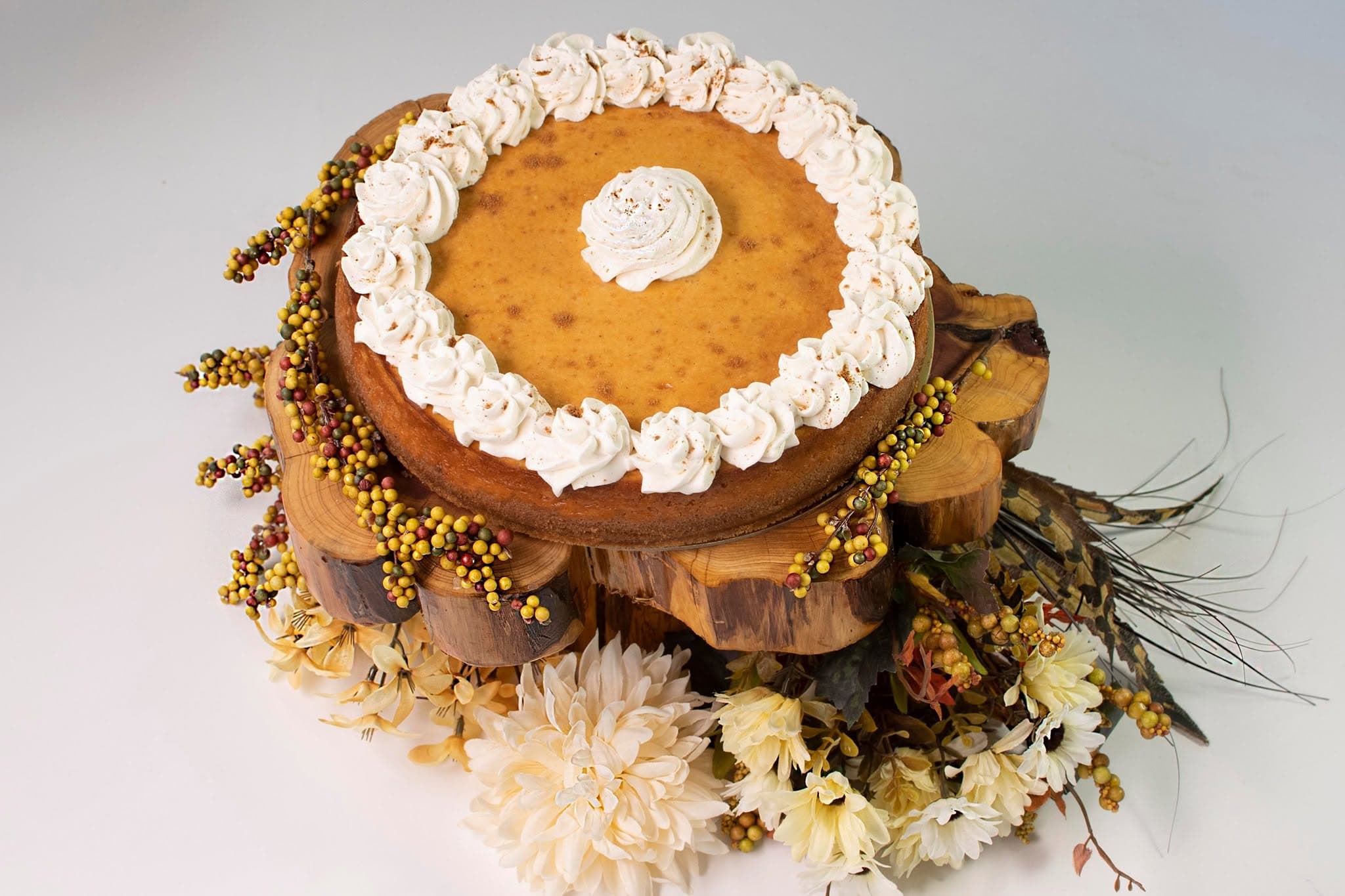 A pumpkin pie displayed on a rustic wood stand with florals, by Something Sweet LLC
